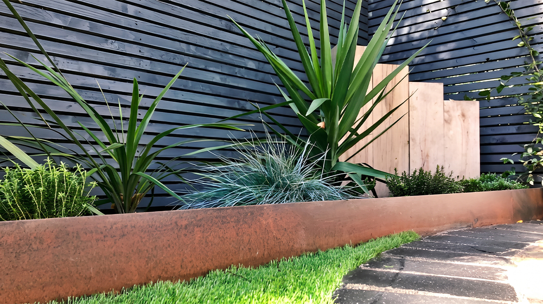 Bordure en acier Corten délimitant avec précision un massif végétalisé et une pelouse dans un jardin contemporain.