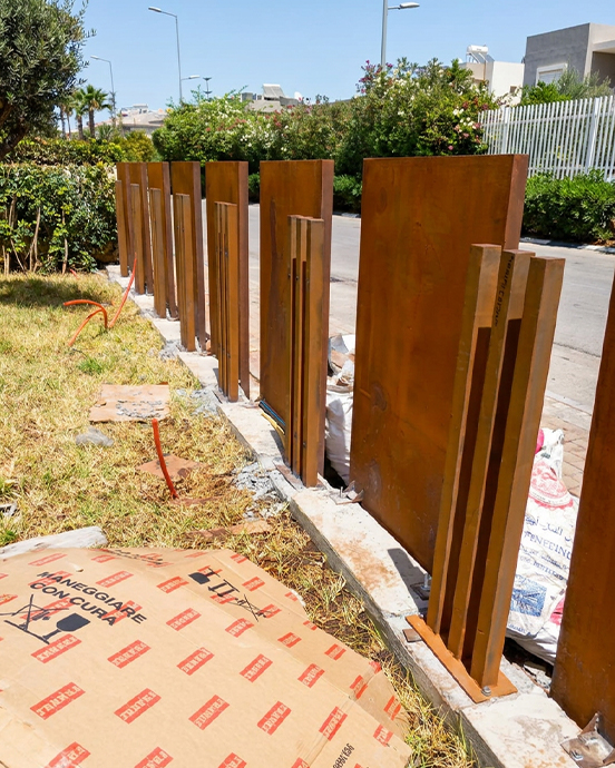 Éléments de clôture verticale en acier Corten en cours d’installation dans un aménagement extérieur résidentiel.