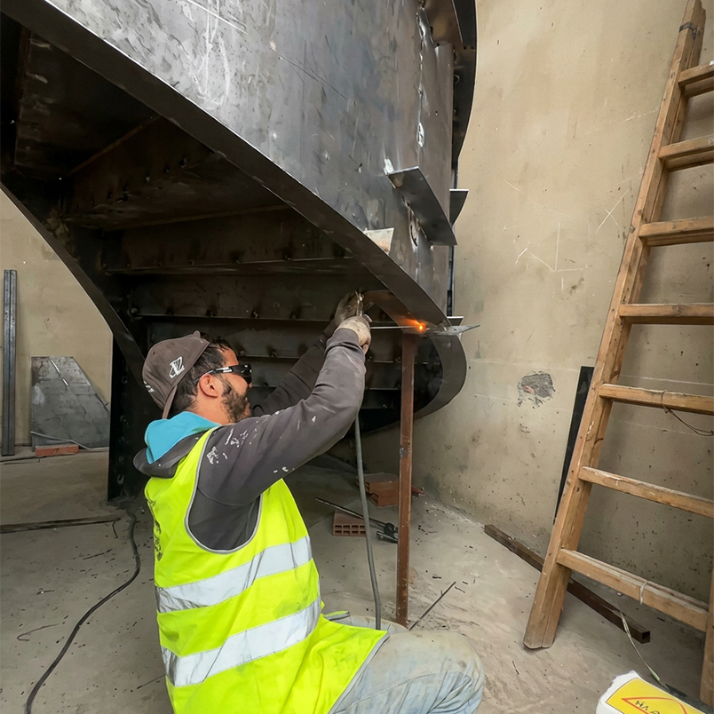 Artisan réalisant les travaux de soudure et d’assemblage d’un escalier métallique sur mesure dans un atelier au Maroc.