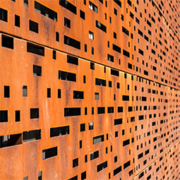 Façade en acier Corten composée de panneaux perforés de motifs carrés et rectangulaires réalisés par découpe laser.