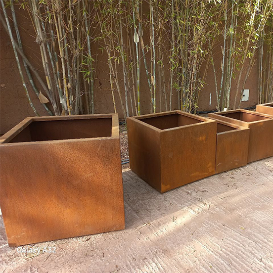 Jardinières carrées en acier Corten présentant une patine orangée vive durant les premiers mois de leur oxydation naturelle.