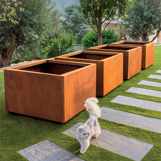 Alignement de jardinières en acier Corten dans un jardin, avec une patine brune mature et stabilisée après une exposition prolongée.