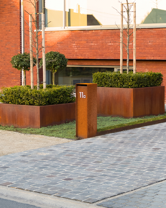 Jardinières rectangulaires et totem d’adresse en acier Corten intégrés à l’entrée paysagère d’une résidence.