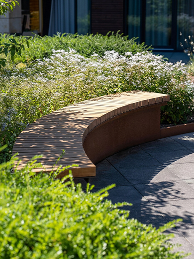 Banc courbe en acier Corten avec assise en bois intégré dans un jardin paysager moderne pour un aménagement extérieur haut de gamme.