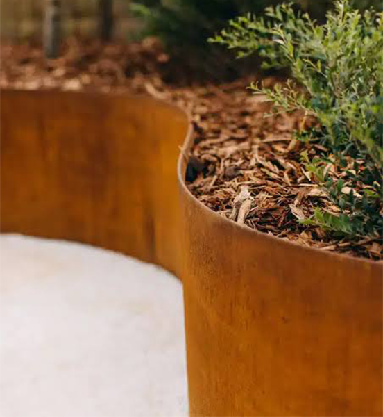 Bordure courbe en acier Corten dessinant un massif végétalisé aux formes organiques dans un jardin contemporain.