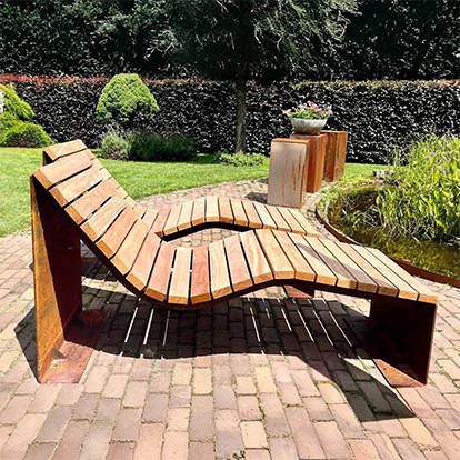 Chaise longue aux formes courbes fabriquée en acier Corten avec une assise en bois, installée dans un jardin paysager.