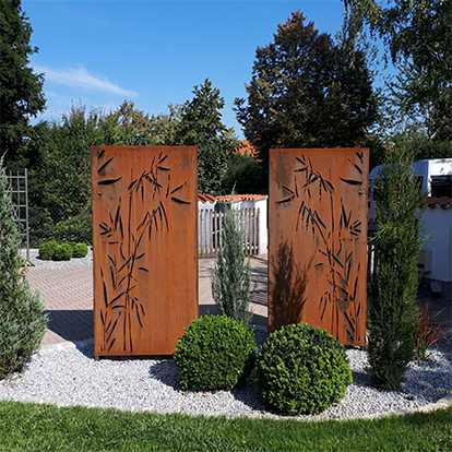 Deux claustras décoratifs en acier Corten découpés de motifs de bambou et intégrés dans un jardin contemporain.