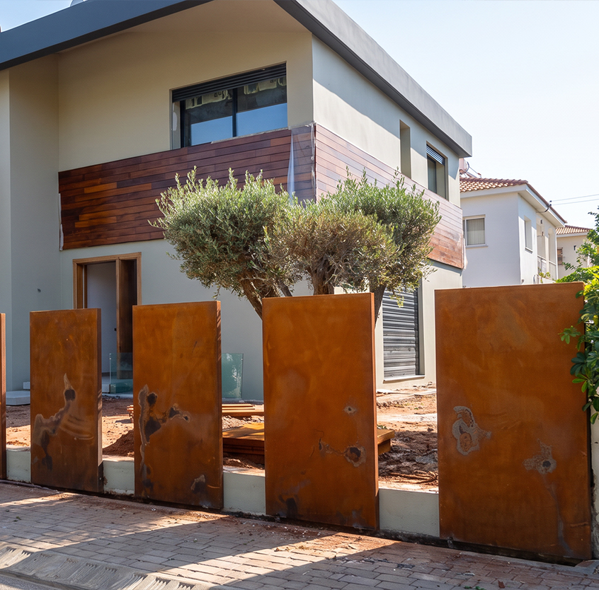 Clôture extérieure composée de panneaux verticaux en acier Corten installés devant le jardin d’une villa contemporaine.