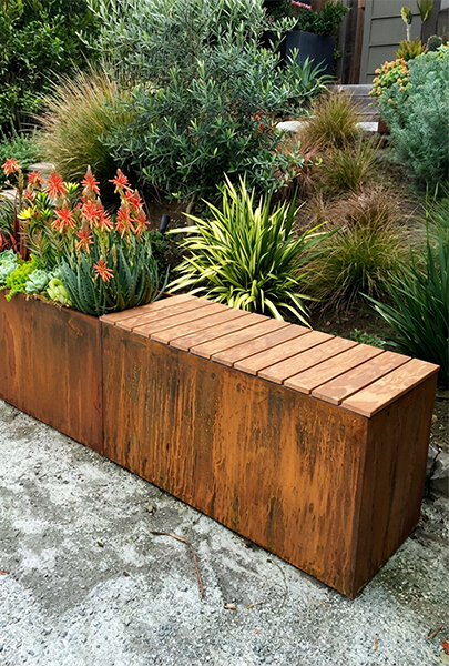 Jardinière rectangulaire en acier Corten avec assise en bois intégrée, installée dans un jardin paysager.