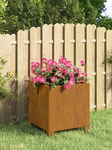Jardinière cubique en acier Corten garnie de fleurs roses et installée dans un jardin résidentiel.