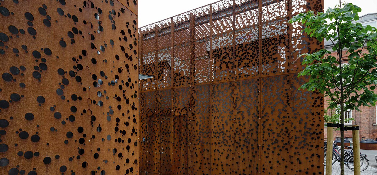 Panneaux architecturaux en acier Corten perforés de motifs circulaires, intégrés à un aménagement extérieur contemporain.