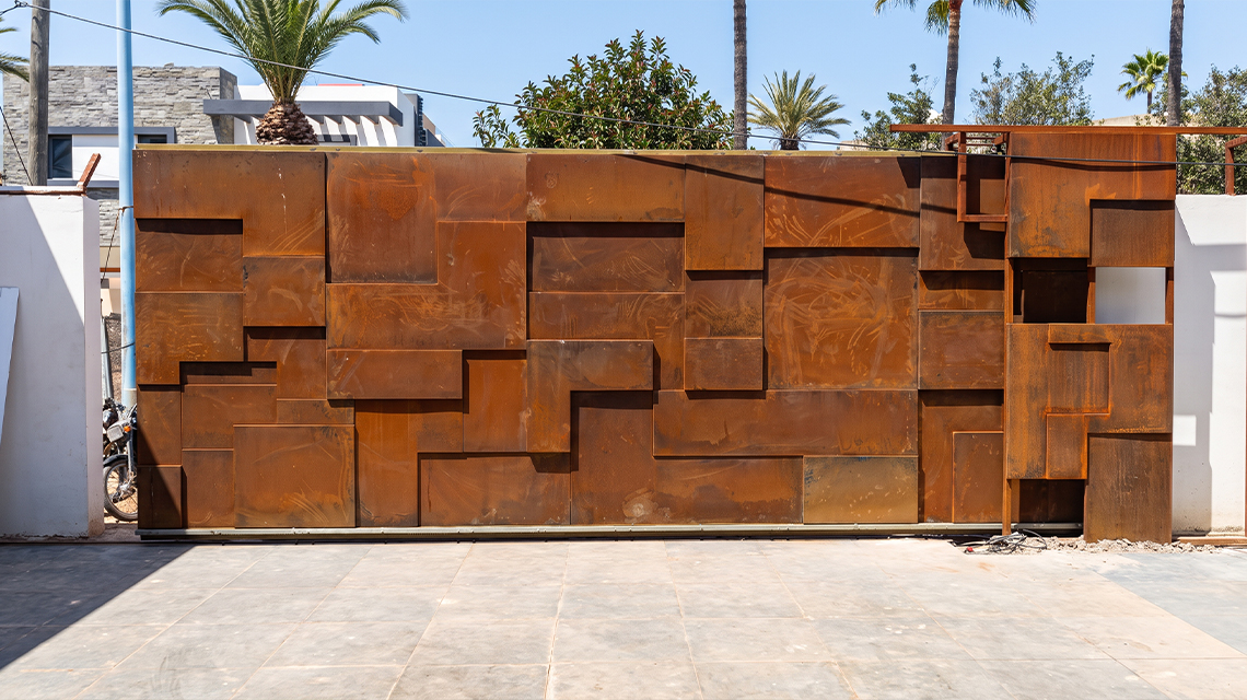 Grand portail en acier Corten composé de volumes géométriques en relief pour une entrée résidentielle contemporaine.
